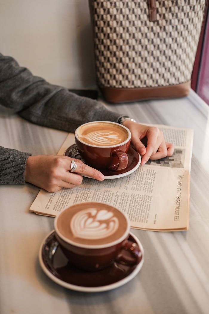 Close-up of two cappuccinos and a newspaper on a marble table, creating a cozy café vibe.